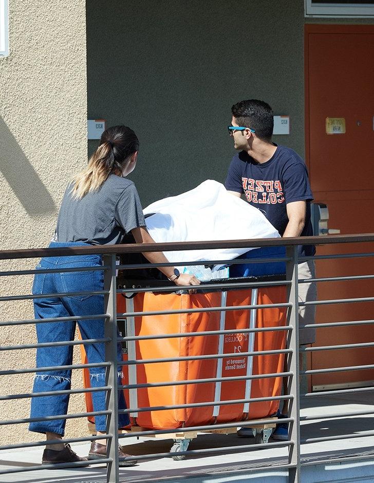 two students use a cart to move items into a dorm room